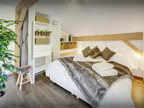 Un dormitorio con una cama grande, techo de madera, armario blanco y un taburete pequeño.