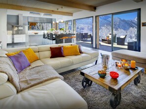 Una sala de estar moderna con un sofá grande, un comedor y vistas a un paisaje montañoso nevado a través de amplios ventanales.