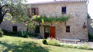 Un bâtiment en pierre avec une porte en bois, des fenêtres et un petit jardin.