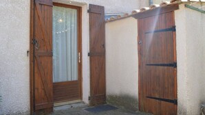 A building with two wooden doors, one with a glass panel, and a tiled roof. - Cozy 4BR House, 750m from Beach, Sleeps 8, Pet-Friendly, Terrace, Parking, WiFi Optional (Fleury-Saint-Pierre-la-Mer)