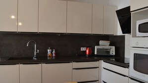 A compact kitchen with a sink, microwave, and stove. - Cozy 4BR House, 750m from Beach, Sleeps 8, Pet-Friendly, Terrace, Parking, WiFi Optional (Fleury-Saint-Pierre-la-Mer)