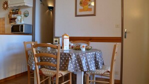 A small dining area with a table covered by a polka dot tablecloth, two wooden chairs, a microwave, and a cabinet with kitchen items. - Saint Pierre la Mer, 2-room appt, cabin, sleeps 6, near beach, pets allowed (Fleury-Saint-Pierre-la-Mer)