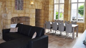 Una sala de estar con un sofá negro, una chimenea, paredes de piedra y una zona de comedor con mesa y sillas.