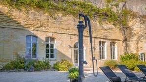 Un edificio de piedra con ventanas arqueadas, una bomba de agua y asientos al aire libre.