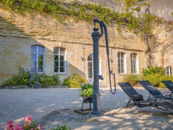 A stone building with arched windows, a water pump, and outdoor seating.