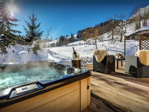 A hot tub on a wooden deck with a snowy landscape in the background.