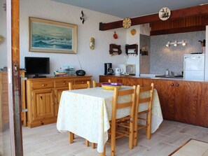 Una cocina acogedora con armarios de madera, una mesa de comedor con sillas, un televisor y diversos electrodomésticos.