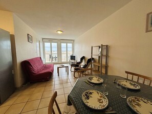 Ein Essbereich mit Tisch für zwei Personen, einem roten Sofa und einem Fernseher im Hintergrund.