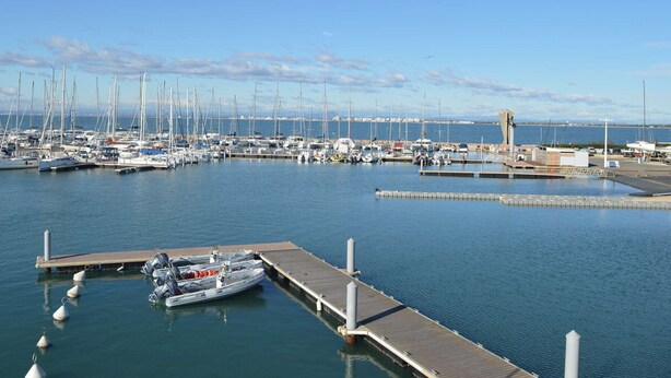 Un puerto deportivo con varias embarcaciones amarradas, un muelle y un cielo despejado.