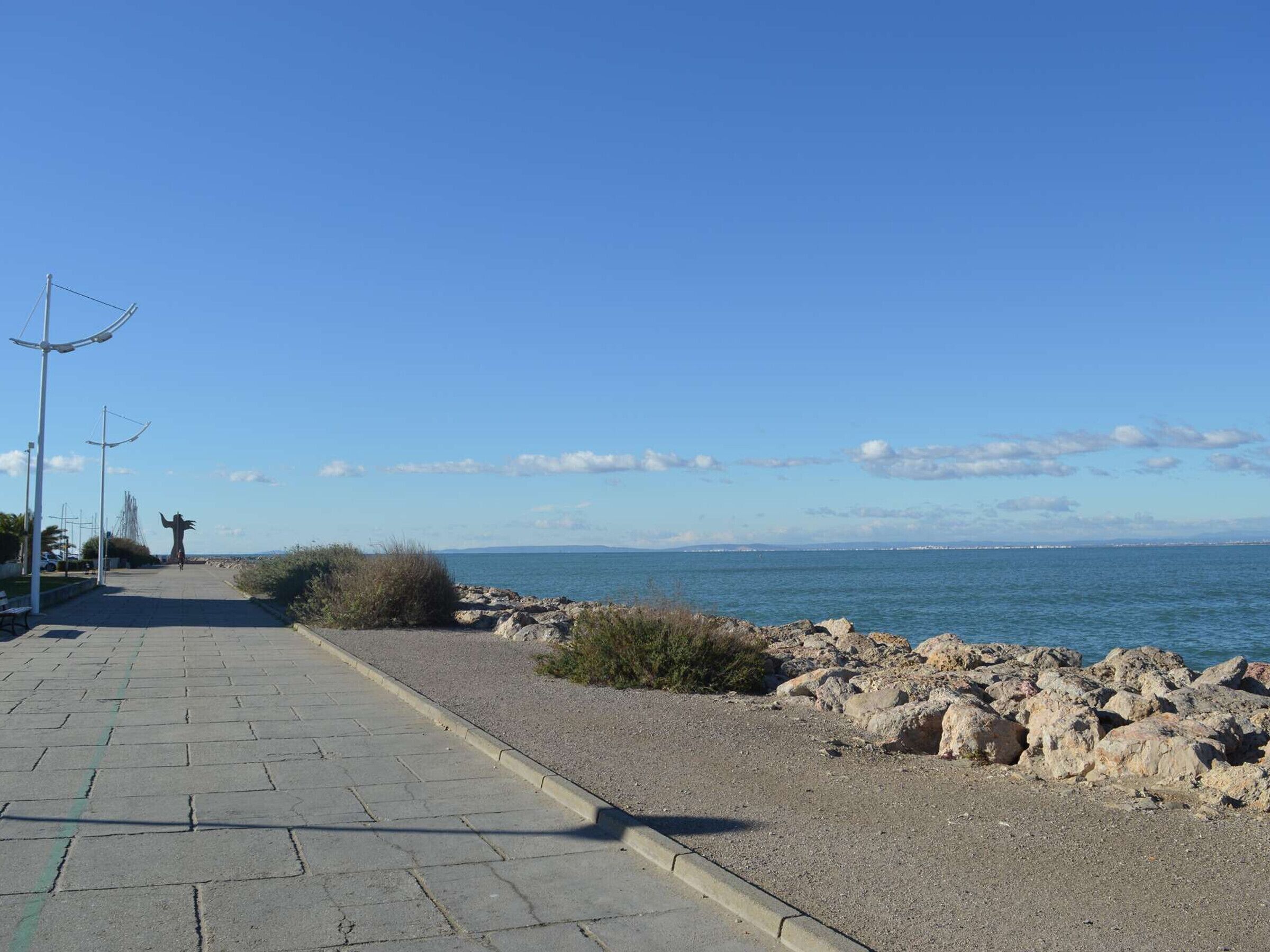Un sentier pavé longe une côte rocheuse, offrant une vue dégagée sur la mer et le paysage urbain lointain.