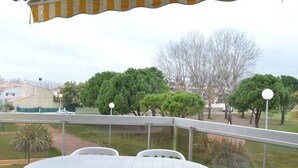 Un patio con una mesa y sillas blancas, con vista a un parque con árboles y un edificio al fondo.