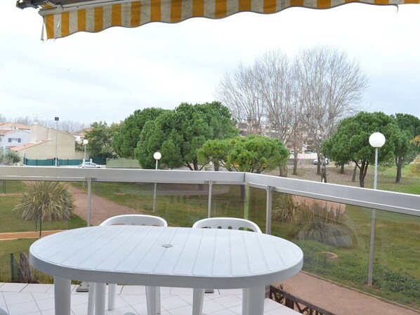 A patio with a white table and chairs, a view of a park with trees and a building in the background.