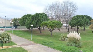 Un parque con un sendero pavimentado, césped verde y diversos árboles.