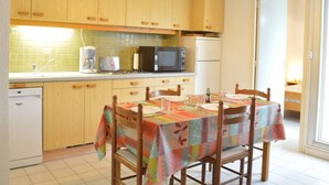 Una cocina compacta con armarios de madera, microondas, refrigerador y una mesa de comedor para cuatro.