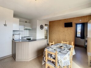 A compact kitchen with a built-in stove and oven, a small island with a microwave, and a dining area with a table and chairs. - Bright apartment 35m², 5 pers, south balcony, near slopes, parking, wifi (La Toussuire)