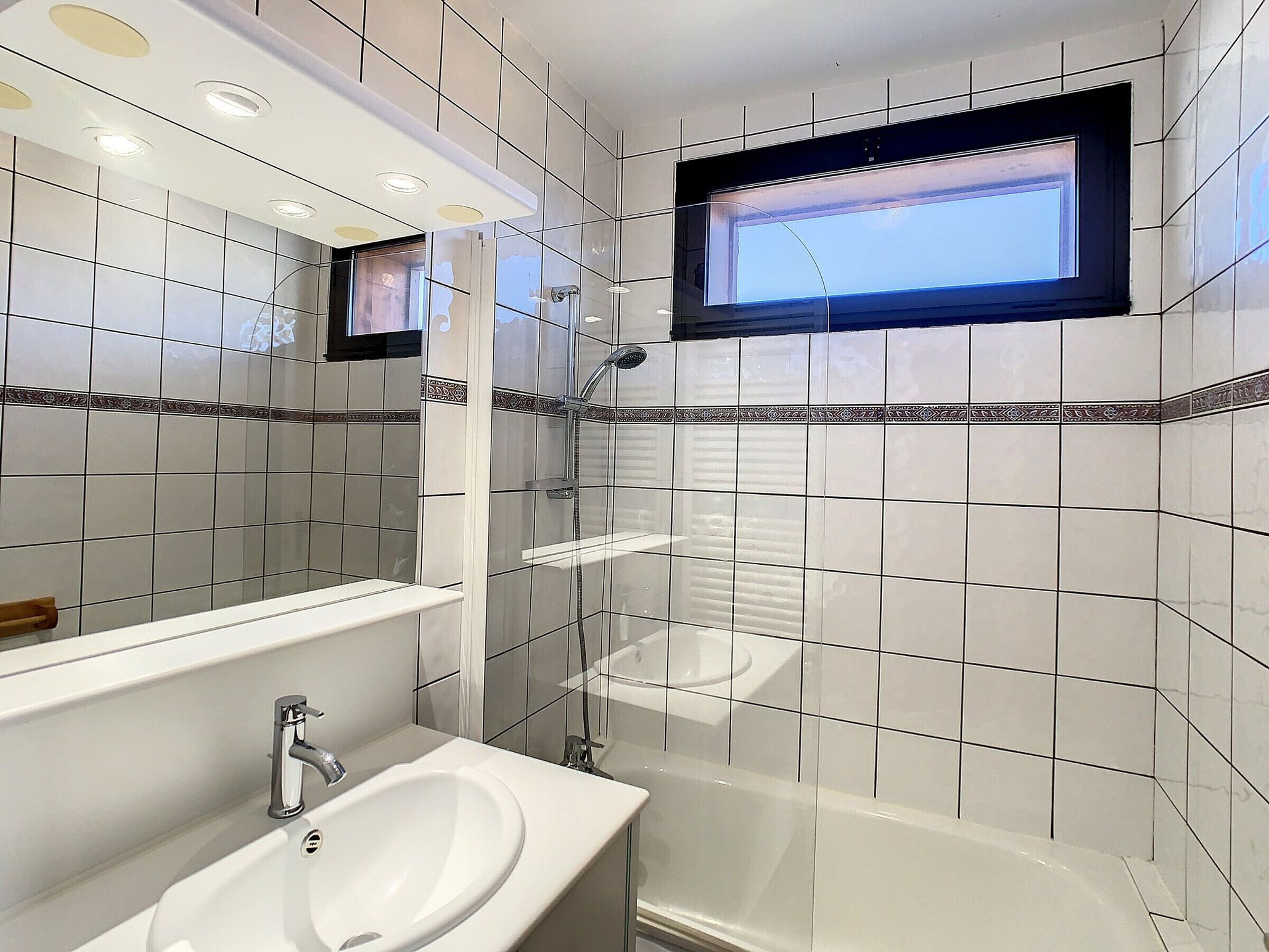 Une salle de bain moderne avec un grand miroir, un lavabo, une douche et une fenêtre.