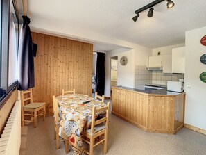 Eine kompakte Küche mit Holzelementen, ein Essbereich mit einem gemusterten Tischlein und ein Klavier in der Ecke.
