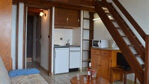 A compact kitchen with a microwave, sink, and cabinets. A wooden staircase leads to another level. - Studio with mezzanine for 5, near the beach, pets allowed - Saint Pierre la Mer (Fleury-Saint-Pierre-la-Mer)