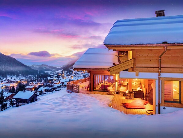 Un chalet en bois doté d’un balcon donnant sur un village enneigé et des montagnes.