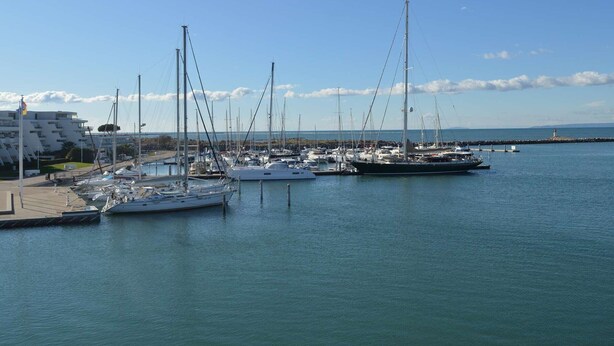 A marina with multiple sailboats docked, a pier, and a building with balconies. - Cozy 4-Sleeper with A/C, Terraces & Direct Marina Access (Port Camargue)