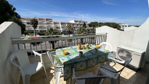 A balcony with a table set for two, white plastic chairs, and a Mitsubishi air conditioner. - Cozy 4-Sleeper with A/C, Terraces & Direct Marina Access (Port Camargue)