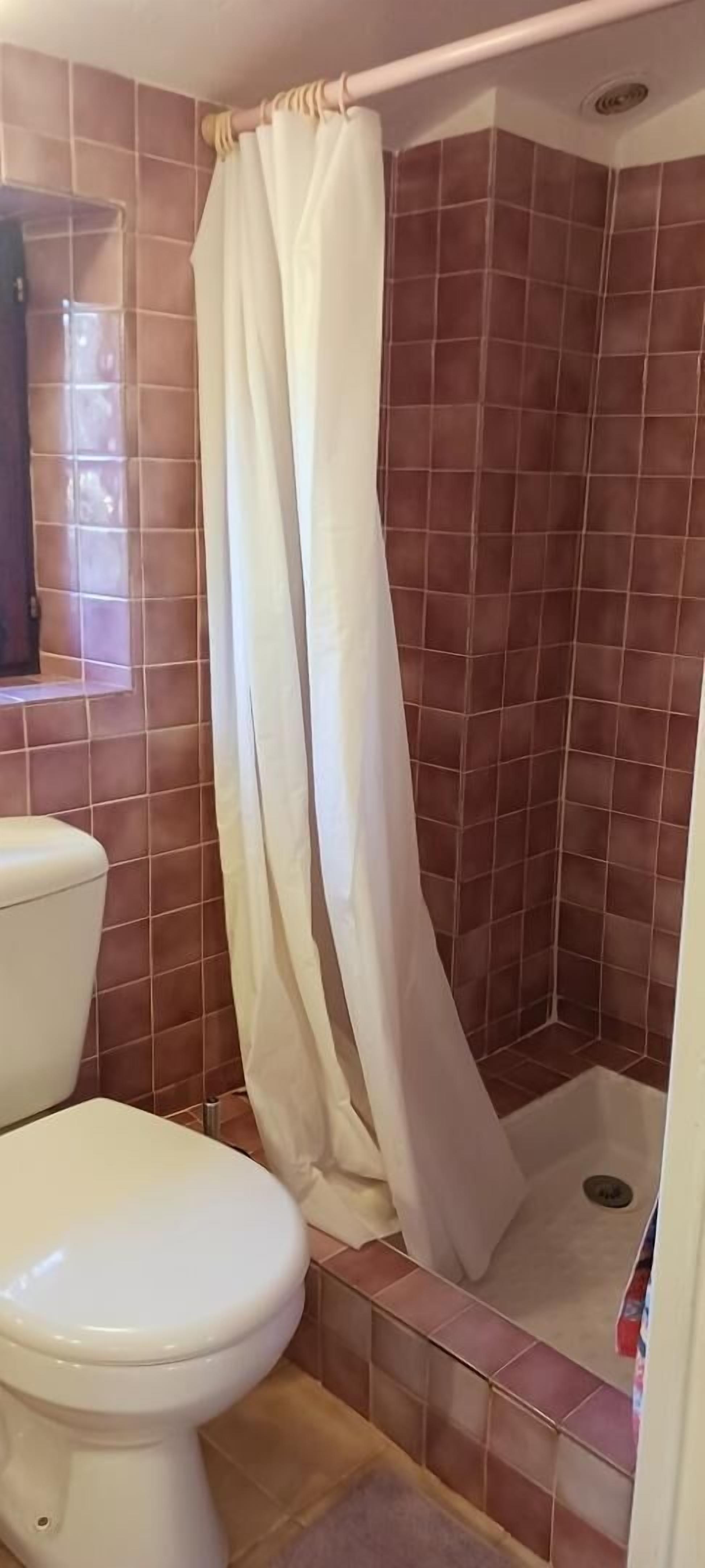 A bathroom with a shower, a toilet, and brown-tiled walls.