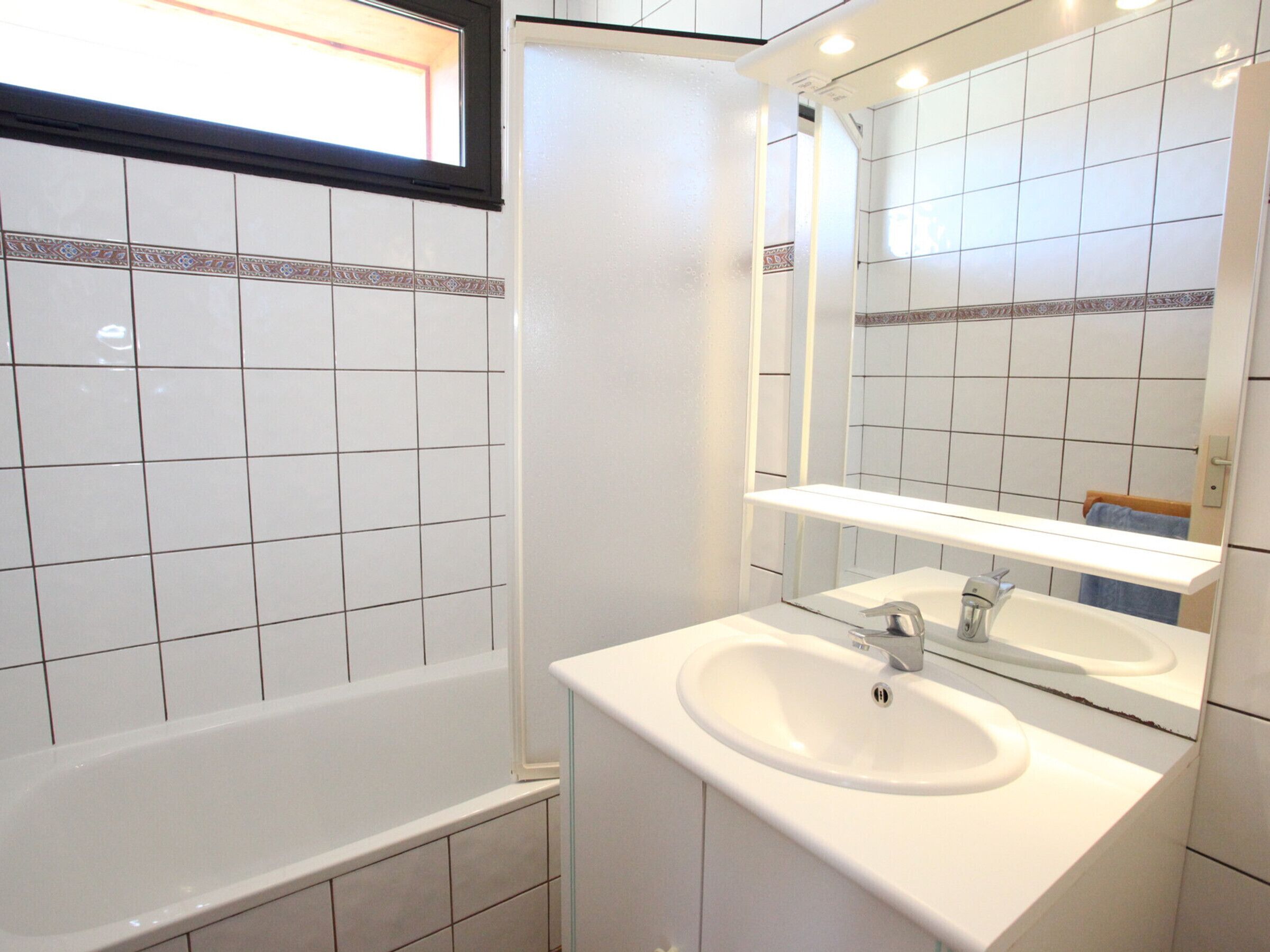 Ein Badezimmer mit weißen Fliesen, einer Badewanne, einem Waschbecken und einem Spiegel.