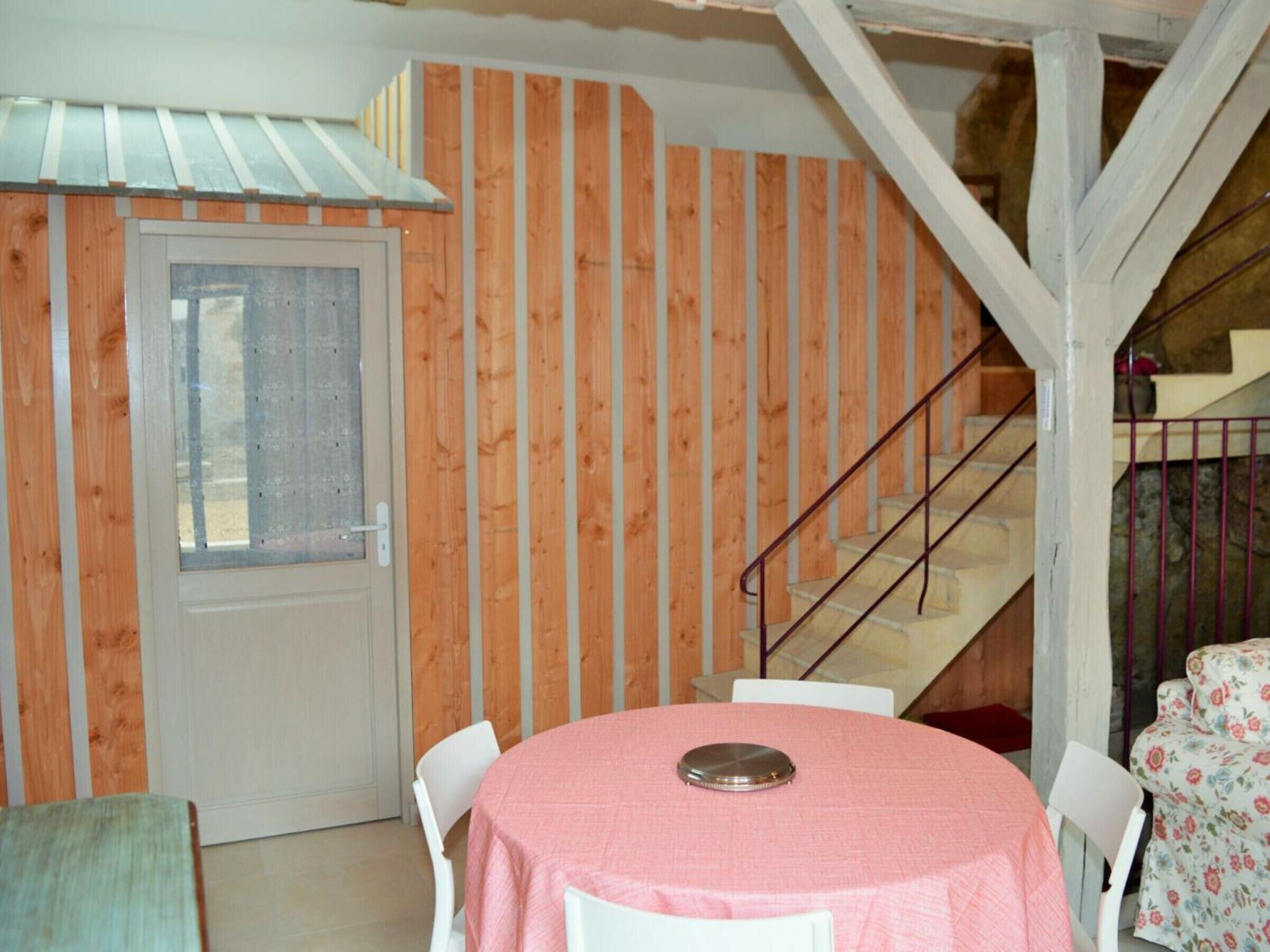 Ein Zimmer mit einer Holzwand, einer weißen Tür, einer Treppe und einem runden Tisch mit rosa Tischdecke.