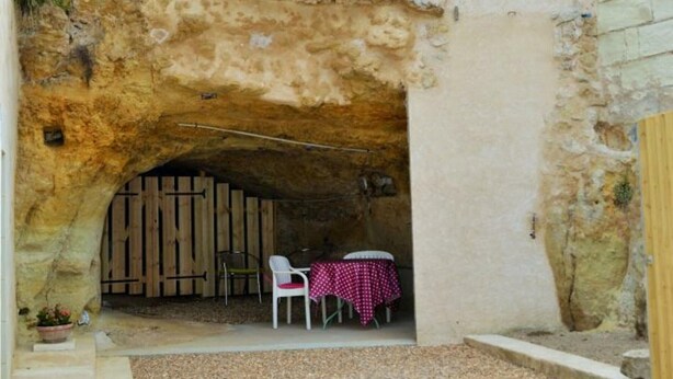 Un espacio de estar al aire libre con un arco rústico de piedra, muebles de madera y una mesa con mantel a cuadros.
