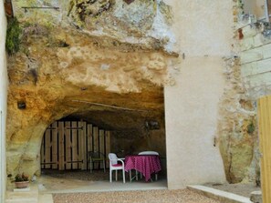 An outdoor seating area with a rustic stone archway, wooden furniture, and a table with a checkered tablecloth. - Unique cottage with garage and private courtyard in Touraine (Savonnières)