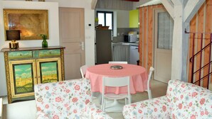 Un comedor con una mesa redonda y sillas de estampado floral, un aparador con obras de arte enmarcadas, y una cocina visible a través de una puerta abierta.