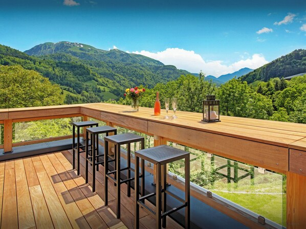 Une terrasse en bois avec des tabourets de bar, un vase de fleurs, une bouteille et des verres.