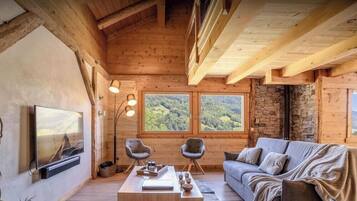 A cozy wooden interior with a TV, two armchairs, a sofa, and a coffee table.