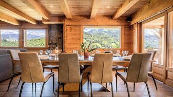A wooden dining room with a table set for four, large windows with mountain views, and a stone fireplace.