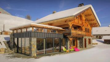 A wooden chalet with a balcony, stone walls, and a snow-covered roof.