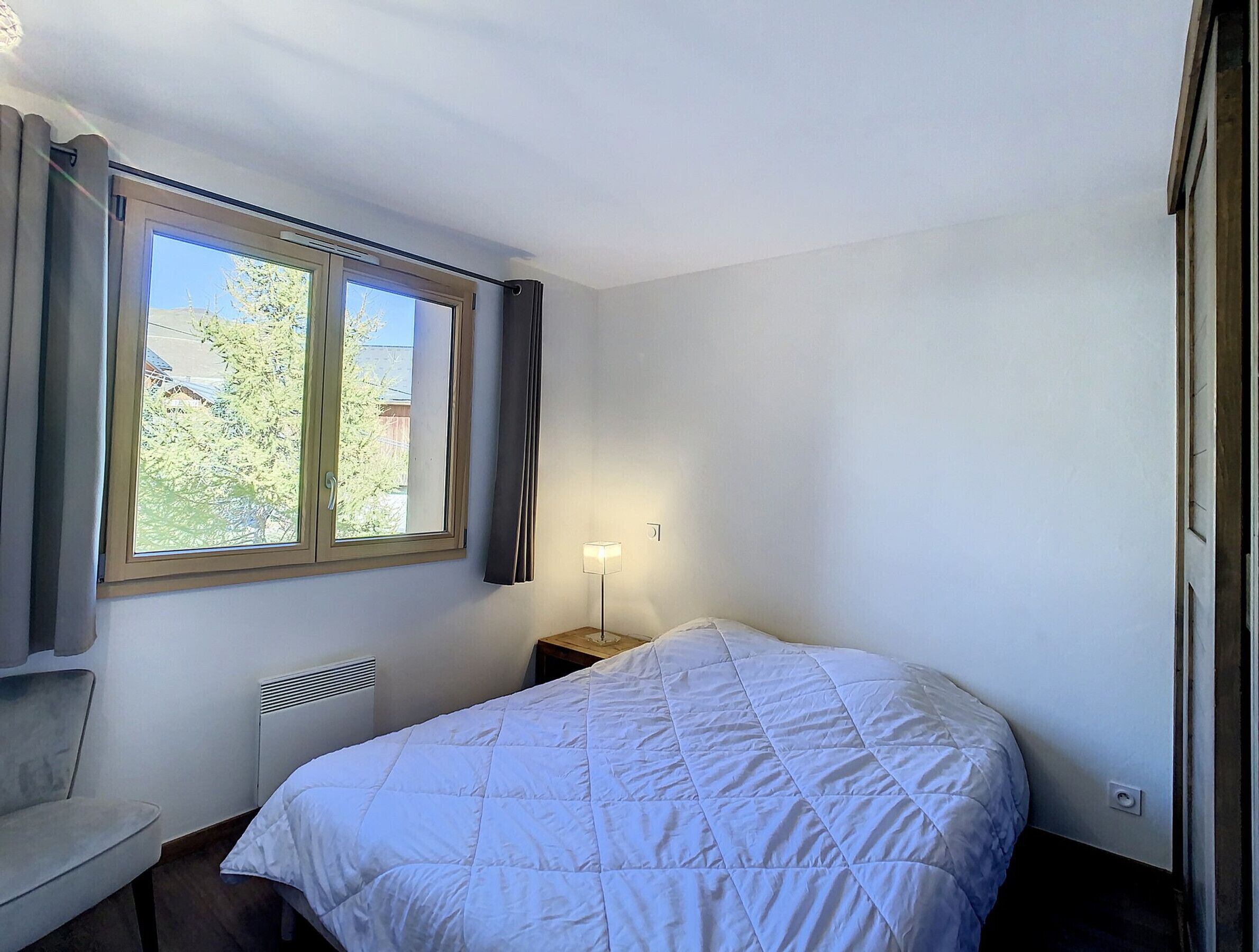 A bedroom with a bed, a window, a bedside table, and a chair.
