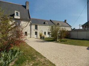 A stone house with a gravel driveway and a small garden with red flowers. - Comfortable lodging in Huismes, near Chinon with enclosed courtyard (Huismes)