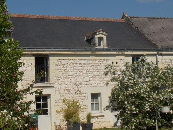 A stone building with a tiled roof, a small dormer window, and a visible door.