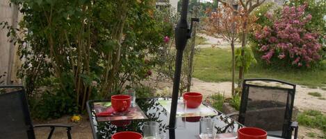 Un área de comedor al aire libre con una mesa dispuesta para dos personas, rodeada de follaje y plantas con flores.