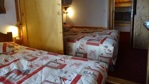 Una habitación con dos camas, una puerta de madera, una lámpara de pared y una cama literera al fondo.