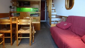 Un espacio habitable compacto con kitchenette, muebles de madera, un sofá rojo y un espejo.
