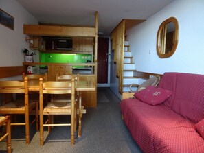 A compact living space with a kitchenette, wooden furniture, a red sofa, and a mirror.