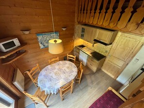 Une cuisine compacte comprenant une table à manger, des chaises en bois, un four à micro-ondes, un petit évier et un réfrigérateur.