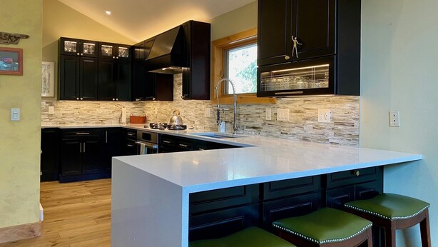 A modern kitchen with dark cabinetry, a large island with bar stools, and a stone backsplash. - 260+ 10★ Reviews!  Between Vail & Beaver Creek Hot Tub/Fire Table/Ski/Hike/ Golf (Vail)