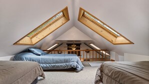 Ein Schlafzimmer mit zwei Betten, einer geneigten Decke und Dachfenstern.