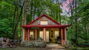 Ein rustikales Steinhaus mit rotem Dach, beschriftet mit „Deer Hunter's Point“, umgeben von dichtem Wald.