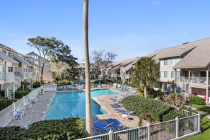 Una piscina con sillas de descanso y palmeras, rodeada de edificios de apartamentos.
