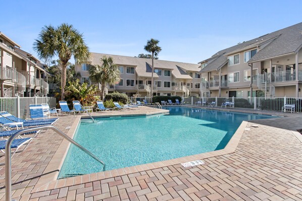 A swimming pool with lounge chairs and palm trees, surrounded by multi-story buildings with balconies.