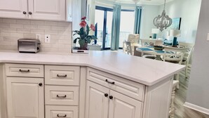 A modern kitchen with white cabinetry, a built-in toaster, and a large window with curtains. - Gorgeous Gulf Views From This Orange Beach Condo on the 11th Floor! (Orange Beach)