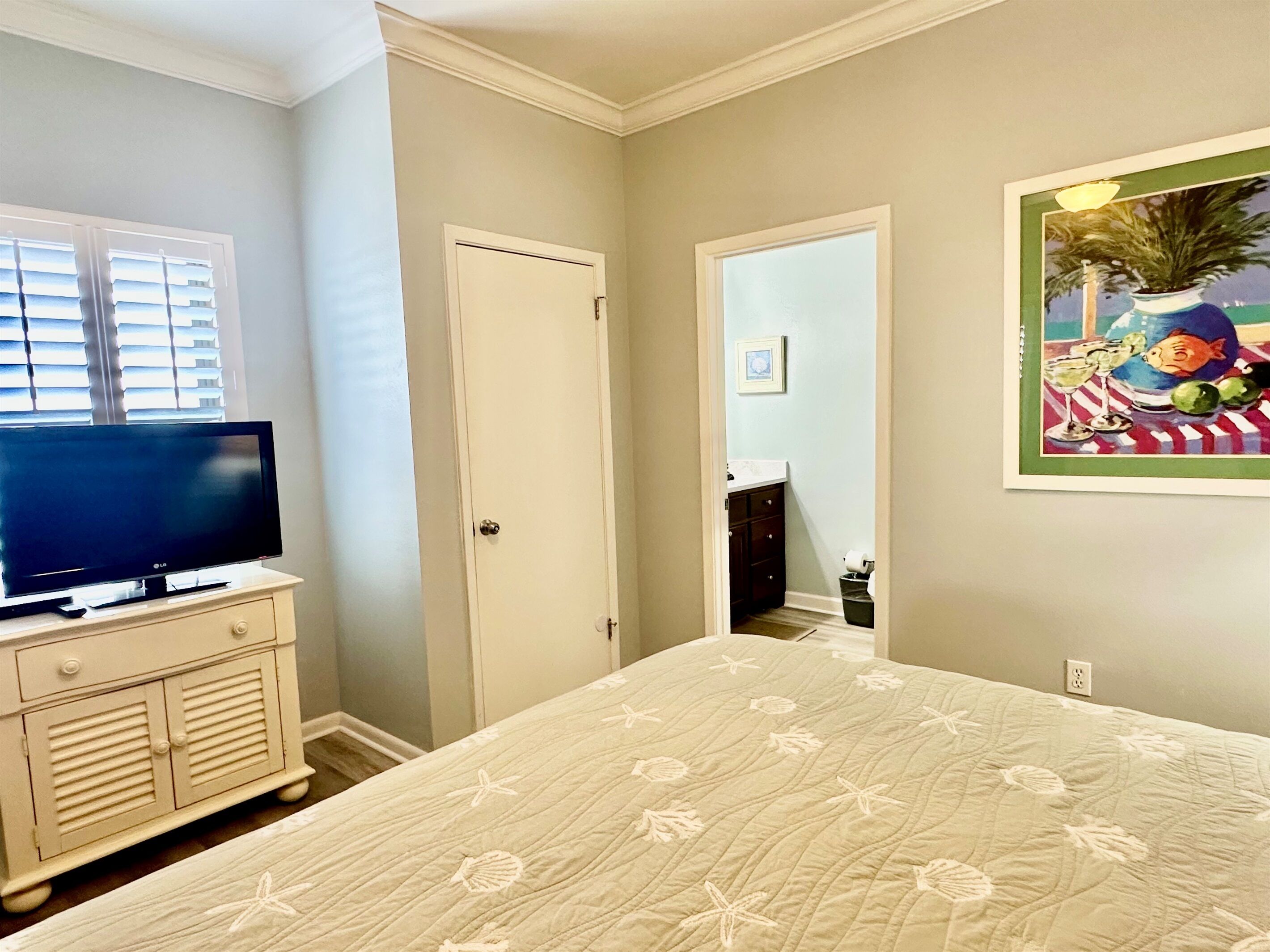 A bedroom with a bed, a television on a dresser, a door, and a painting on the wall.